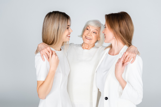 drei Generationen fröhlicher Frauen lächeln, während sie sich isoliert auf grau umarmen - Foto, Bild