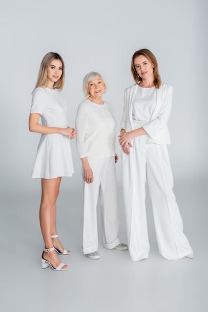 volledige lengte van drie generatie gelukkige vrouwen glimlachend terwijl ze op grijs staan - Foto, afbeelding