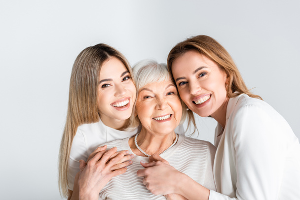 trzy pokolenia pozytywnych kobiet uśmiechających się patrząc w kamerę i przytulając odizolowane na szaro - Zdjęcie, obraz