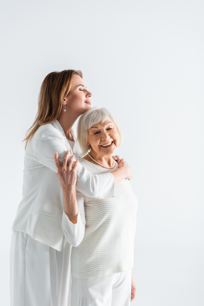 felice figlia abbracciando la madre anziana con i capelli grigi isolati su bianco - Foto, immagini