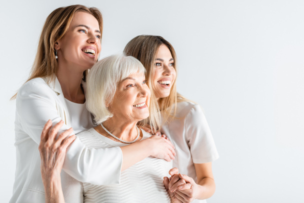 three generation of positive women smiling while hugging isolated on white - Photo, Image
