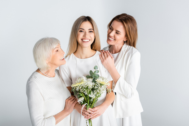 cheerful young woman smiling while holding flowers near mother and granny isolated on grey - Zdjęcie, obraz