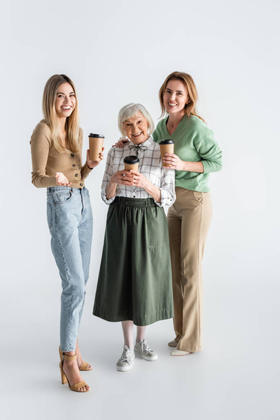 full length of three generation of happy women holding paper cups on white - Fotografie, Obrázek