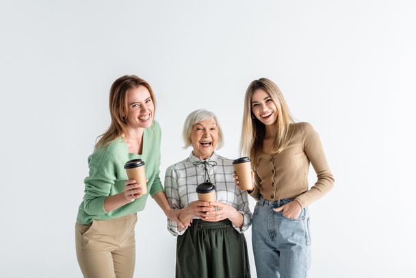 three generation of cheerful women holding paper cups isolated on white - Photo, image