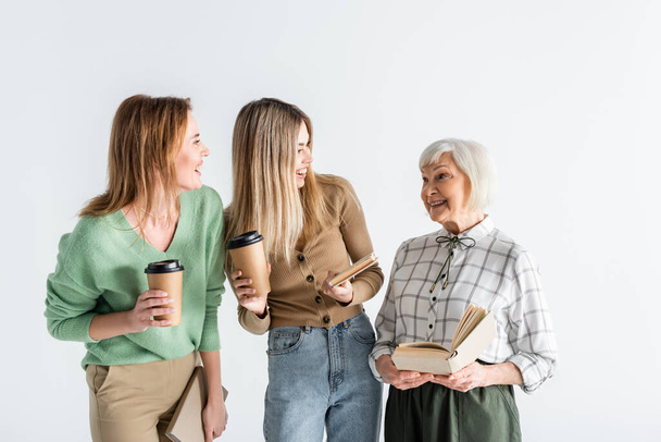 three generation of happy women holding paper cups and books isolated on white - Fotografie, Obrázek