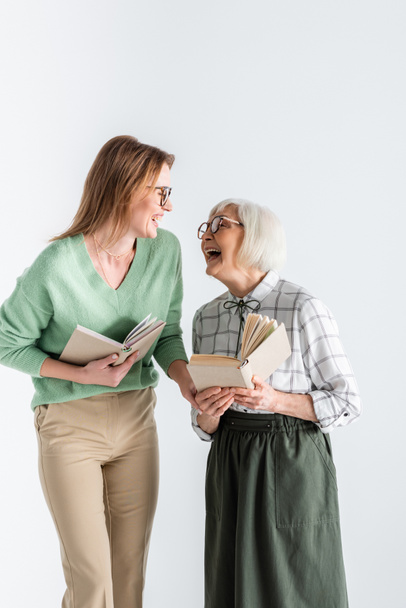 senior mother laughing with daughter in glasses while holding books isolated on white - Φωτογραφία, εικόνα