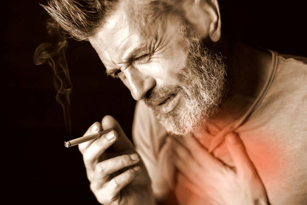 Man smokes cigarette and has problem with lungs in front of black background. Cigarette addiction concept - Foto, Imagem