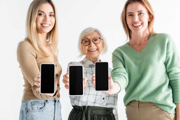 trois générations de femmes heureuses tenant des smartphones avec écran blanc isolé sur blanc - Photo, image