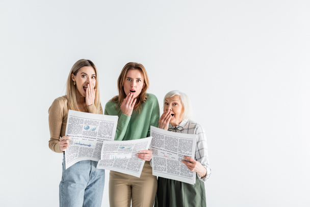 three generation of shocked women holding newspapers isolated on white - Photo, Image