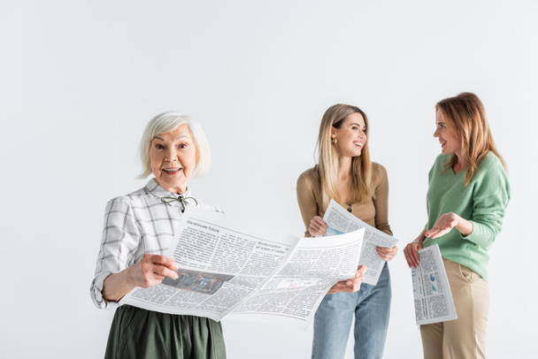 alegre anciana sosteniendo periódico cerca de hija y nieta sobre fondo borroso aislado en blanco - Foto, imagen