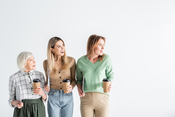 three generation of amazed women holding newspapers and paper cups isolated on white - Foto, immagini