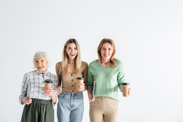 drie generaties opgewonden vrouwen met kranten en papieren bekers geïsoleerd op wit - Foto, afbeelding