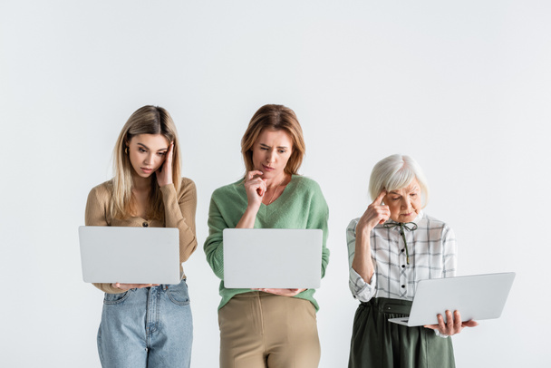 trzy pokolenia zamyślonych kobiet korzystających z laptopów izolowanych na białym - Zdjęcie, obraz