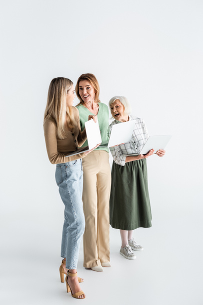 full length of three generation of women holding laptops and smiling on white - Zdjęcie, obraz