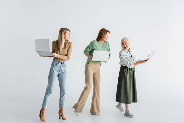 full length of three generation of women with laptops on white - Zdjęcie, obraz