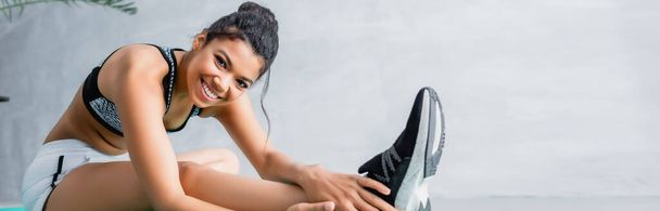 happy african american sportswoman looking at camera while stretching at home, banner - Fotoğraf, Görsel
