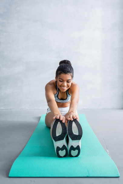 smiling african american sportswoman doing seated forward bend exercise at home - Photo, Image