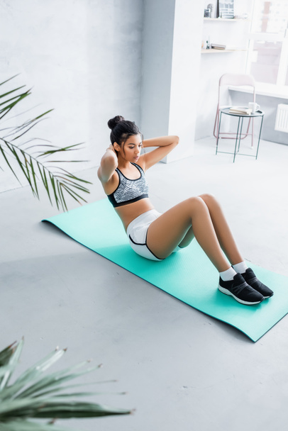 young american woman in sportswear doing abs exercise on fitness mat at home, blurred foreground - Photo, Image