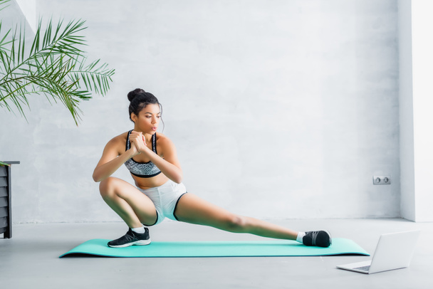 young african american sportswoman doing stretching exercise on fitness man near laptop - Foto, Bild
