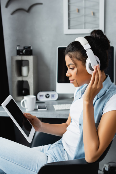side view of african american freelancer in wireless headphones holding digital tablet with blank screen, blurred background - Фото, зображення