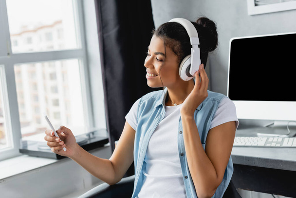 happy african american freelancer messaging on smartphone while listening music in wireless headphones at home - 写真・画像
