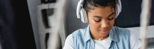 νεαρή Αφροαμερικανή γυναίκα που ακούει μουσική σε ασύρματα ακουστικά στο σπίτι, banner - Φωτογραφία, εικόνα