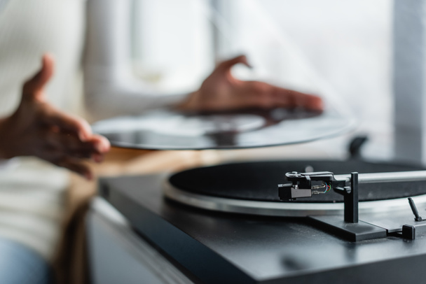 partial view of african american woman holding vinyl disc near record player, blurred background - Foto, Bild