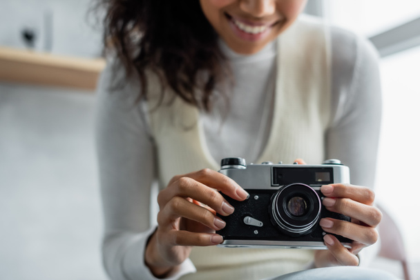 cropped view of smiling african american woman holding vintage photo camera, blurred background - Foto, immagini