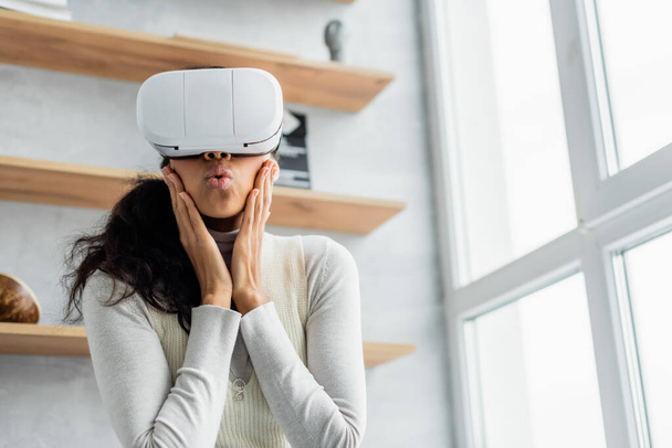 surprised african american woman touching face and pouting lips while gaming in vr headset - Fotoğraf, Görsel