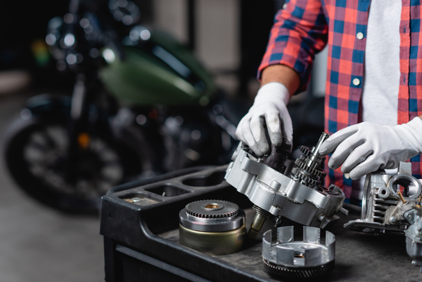 Ausgeschnittene Ansicht eines Reparateurs in Handschuhen bei der Untersuchung eines zerlegten Motorradgetriebes - Foto, Bild