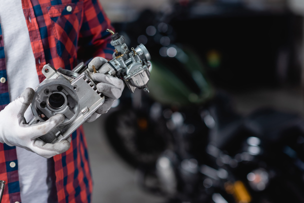 Ausgeschnittene Ansicht eines Mechanikers in Handschuhen, der einen Teil des Motorradgetriebes hält - Foto, Bild