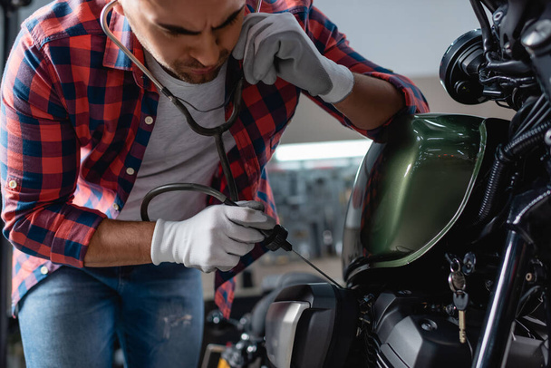 joven mecánico en guantes de control de motor de moto con estetoscopio - Foto, Imagen