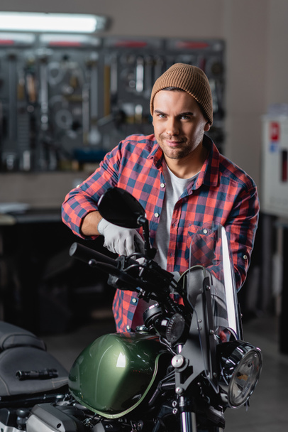 Mecânico sorrindo olhando para a câmera ao fazer o diagnóstico de motocicleta na oficina - Foto, Imagem