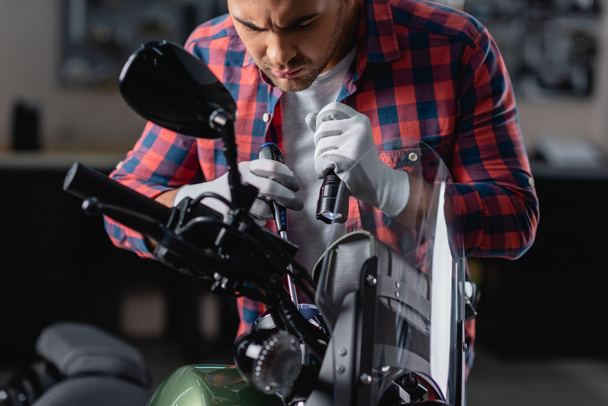 joven reparador sosteniendo linterna y destornillador mientras comprueba moto - Foto, Imagen