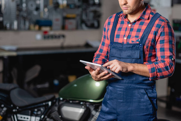 cropped view of technician in overalls using digital tablet in workshop - 写真・画像