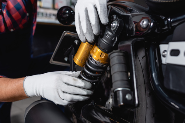 cropped view of mechanic checking shock absorber of motorcycle in workshop - Foto, Bild