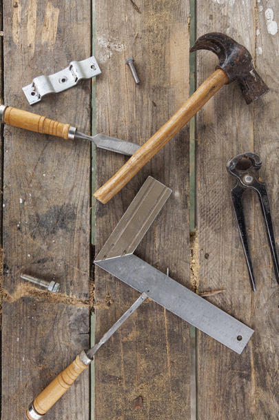 Some carpenter tools on a wooden table. There is a hammer, a pair of pliers, two chisels, a square and screws - 写真・画像