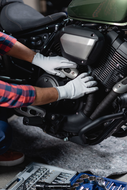 cropped view of repairman in gloves checking motorbike near toolbox in workshop - Фото, изображение