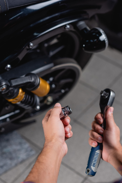 partial view of repairman holding socket wrench near motorbike on blurred background - Photo, Image