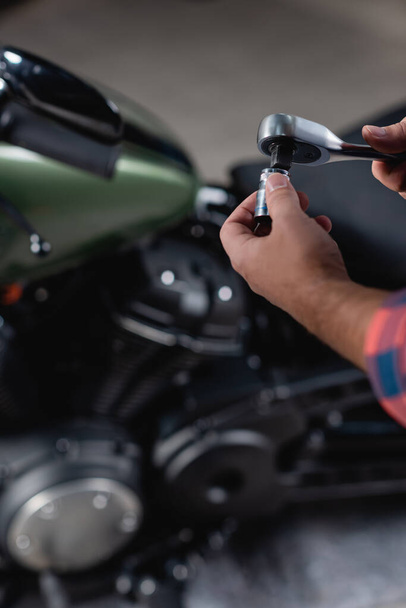 cropped view of technician holding socket wrench near motorcycle on blurred background - Фото, изображение