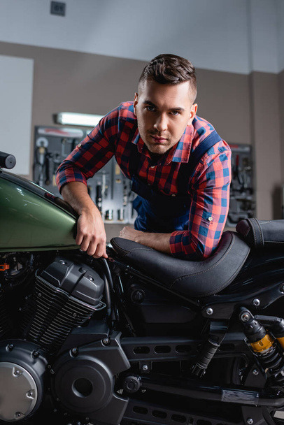 young repairman looking at camera while making diagnostics of motorbike in workshop - 写真・画像