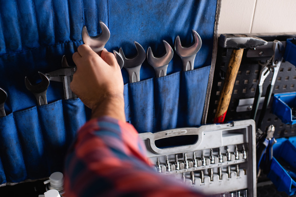 cropped view of mechanic taking wrench from set near toolbox, blurred foreground - Photo, Image