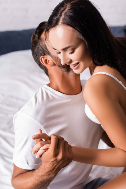 happy brunette woman with closed eyes, holding hands with boyfriend on bed  - Foto, imagen