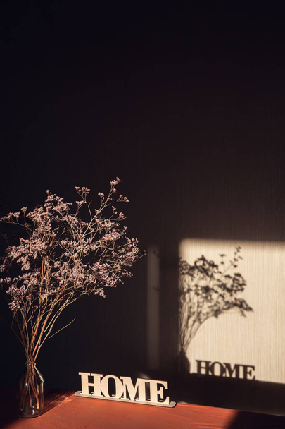 Valo ja varjo ikkunan läpi seinään kirjoitus House ja kuivattu kukkakimppu läpinäkyvä maljakko. - Valokuva, kuva