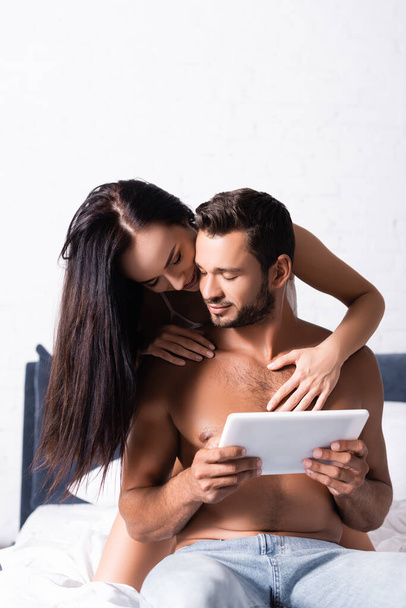 seksikäs brunette nainen viettelee paidaton mies tabletti makuuhuoneessa  - Valokuva, kuva