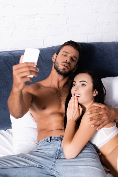 νεαρό σέξι ζευγάρι με smartphone που παίρνει selfie στο κρεβάτι  - Φωτογραφία, εικόνα