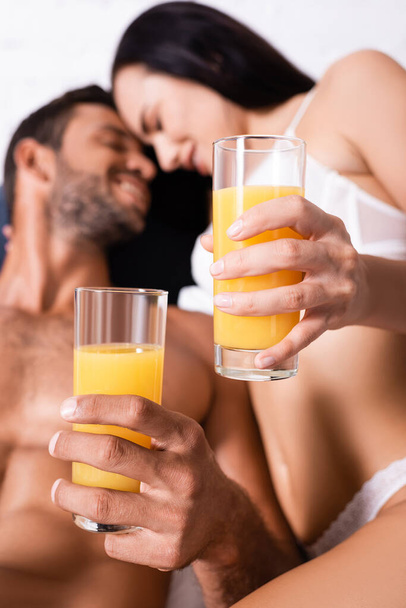 vue rapprochée des verres avec du jus dans les mains d'un jeune couple souriant sur fond flou  - Photo, image