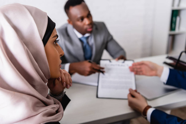 арабська бізнес-леді поблизу мультикультурних ділових партнерів обговорюють контракт на розмитому тлі
  - Фото, зображення