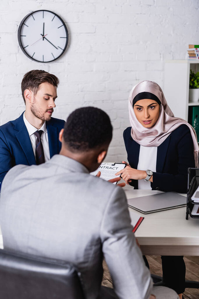 арабська бізнес-леді вказує пальцем за контрактом під час зустрічі з міжрасовими діловими партнерами, розмитий передній план
 - Фото, зображення