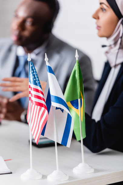 foco seletivo de EUA, Israel e bandeiras brasileiras perto de parceiros de negócios árabes e afro-americanos em fundo turvo - Foto, Imagem